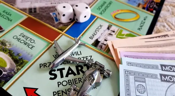 Plansza Monopoly z pionkami (samolot, bolid), kostkami i banknotami.