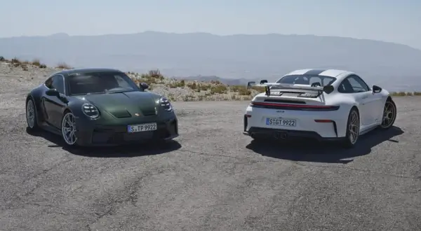 Dwa Porsche 911 GT3, zielone i białe, stoją na górskiej drodze.