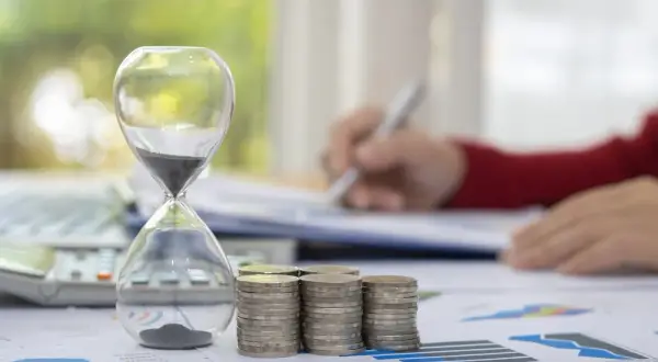 Klepsydra, monety i kalkulator symbolizują czas i finanse. Zastanawiasz się, na ile lat można wziąć kredyt gotówkowy?