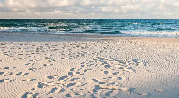 Piasek na plaży, ślady stóp i fale morza. Idealne miejsce, gdzie nad morze.