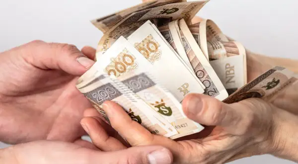 Dwie pary rąk przekazują sobie plik banknotów 200 zł. Może to być darowizna, od której należy zapłacić podatek od darowizny.