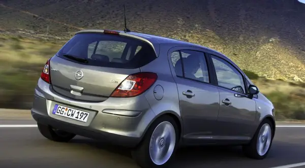 Szary Opel Corsa D 1.2 benzyna w ruchu, z widokiem na tył, na tle górskiego krajobrazu.