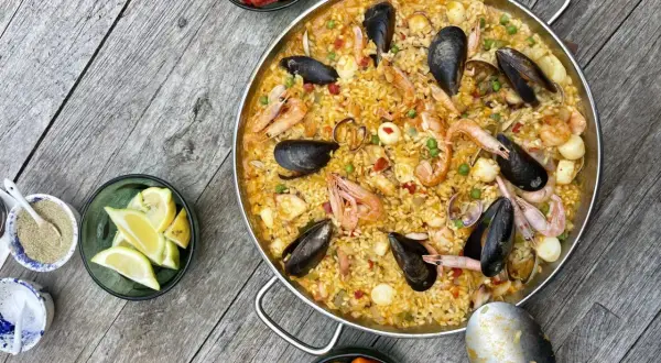 Ein köstliches Paella-Rezept mit Garnelen, Muscheln und Reis, garniert mit Zitronenspalten und Paprika.