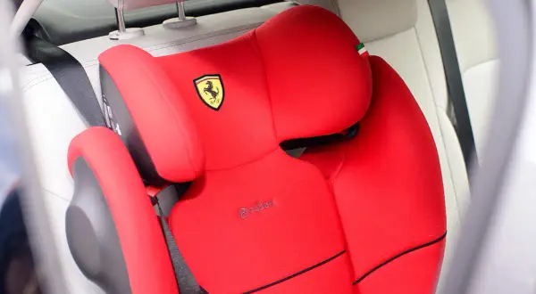 Czerwony fotelik samochodowy Cybex z logo Ferrari. Pasek bezpieczeństwa przechodzi przez fotelik, pokazując, jak prawidłowo zapinać fotelik samochodowy.