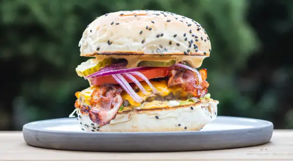 Soczysty burger z bekonem, serem i warzywami na talerzu. Idealny, by pokazać, jak jeść burgera.