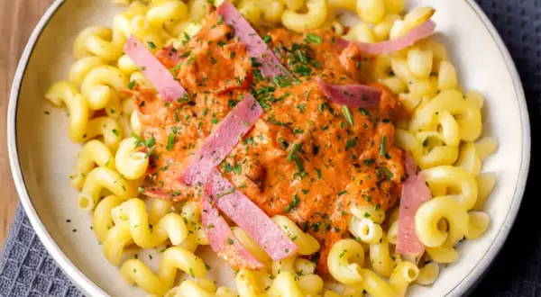 Gedrehte Nudeln mit cremiger Tomatensoße und rosa Wurststreifen, garniert mit Petersilie.