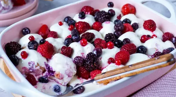 Ein cremiges Windbeutel-Dessert mit frischen Beeren wie Himbeeren, Blaubeeren und Brombeeren in einer rosa Schale.