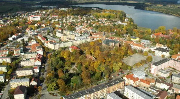 Widok z lotu ptaka na miasto z jeziorem w tle. Widać zabudowania, drzewa w jesiennych barwach i kościół. To największy rynek w Polsce.