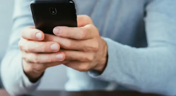 Dłonie trzymające czarny smartfon. Dowiedz się, jak się wylogować z FB na telefonie, by zadbać o prywatność.