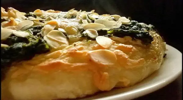 Eine köstliche Spinat Pizza mit knusprigem Teig und gerösteten Mandelblättchen. Dampf steigt auf und verspricht ein warmes, herzhaftes Gericht.