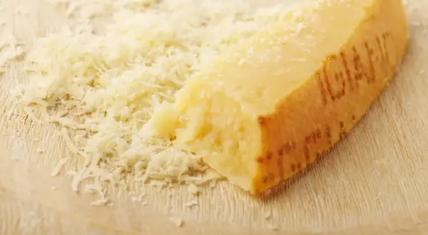 Ein Stück Parmesan mit geriebenem Käse auf einem Holzbrett.
