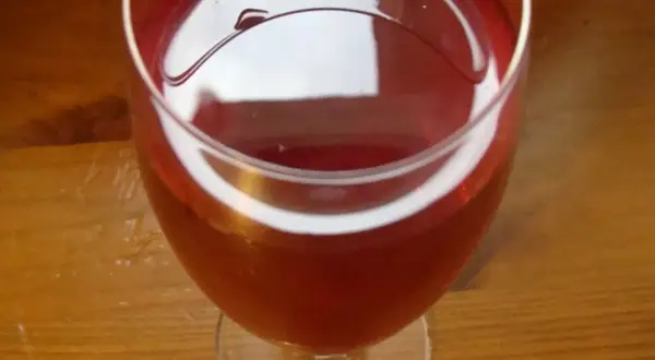 Czerwone wino z róży w kieliszku, na drewnianym stole. Delikatny, rubinowy kolor napoju.