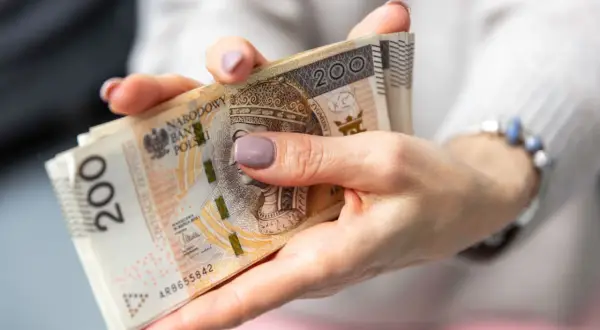 Dłonie trzymające stos banknotów 200 zł. Zastanawiasz się, jak wypłacić pieniądze z PPK?