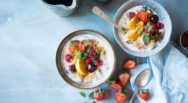 Dwa talerze owsianki z owocami (truskawki, maliny, pomarańcza, marakuja) i gwiazdkami anyżu. Idealne na śniadanie, gdy stawiasz na dieta wysokowęglowodanowa.