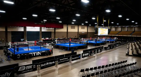 Multiple boxing rings are set up in an arena, ready for competition. A large screen displays a bracket, hinting at the usa boxing weight classes.