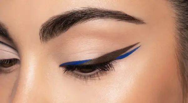 Occhio con eyeliner grafico marrone e blu elettrico, un audace cat crease che cattura lo sguardo.