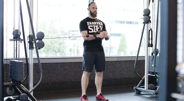 Mężczyzna z brodą wykonuje ćwiczenie pallof press przy użyciu wyciągu.