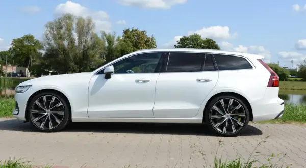 Białe Volvo T6 kombi stoi na tle zieleni i błękitnego nieba.