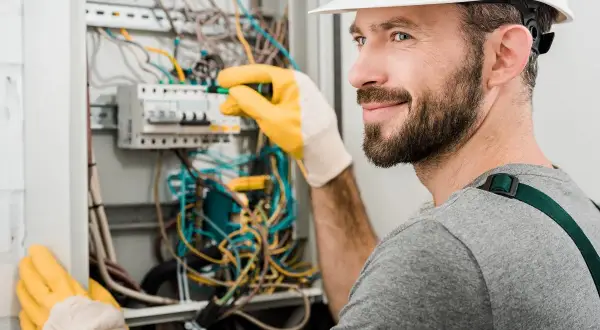 Elektryk z uprawnieniami SEP do 1kV pracuje przy rozdzielnicy, poprawiając okablowanie.