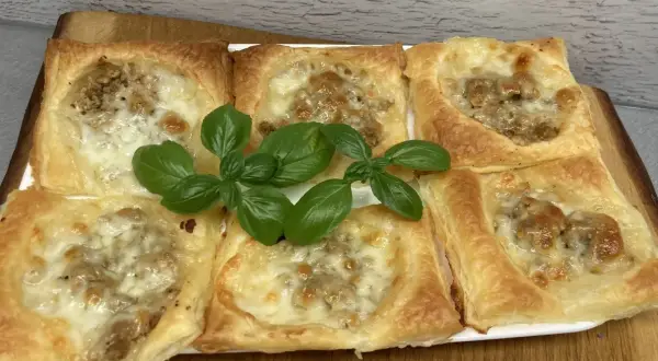 Sześć kwadratowych porcji ciasta francuskiego z mięsem mielonym i serem, ozdobione świeżą bazylią.