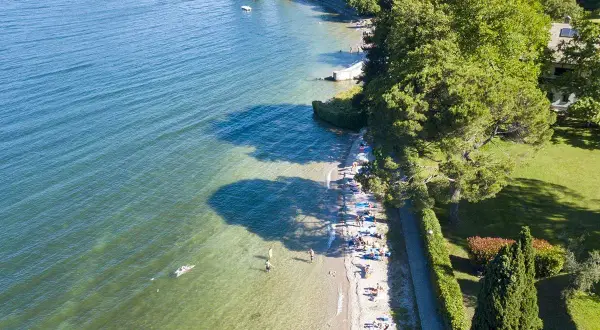Słoneczny dzień nad jeziorem Como. Ludzie odpoczywają na plaży i pływają w krystalicznie czystej wodzie.