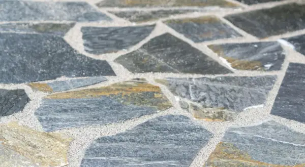 Nahaufnahme von polygonalplatten verlegen. Die unregelmäßigen Steine sind grau und gelblich, mit hellem Sand dazwischen.