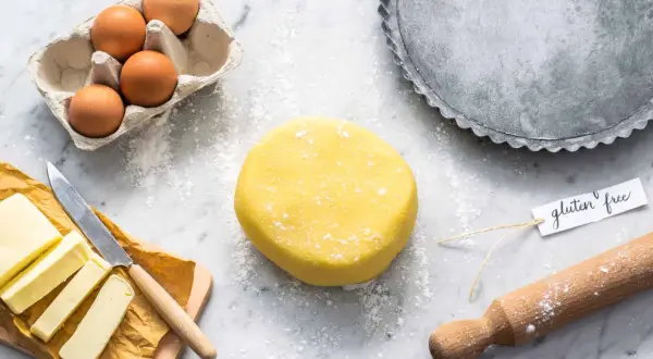 Impasto giallo per pasta frolla senza glutine, uova, burro e stampo per crostata pronti per creare un dolce delizioso.
