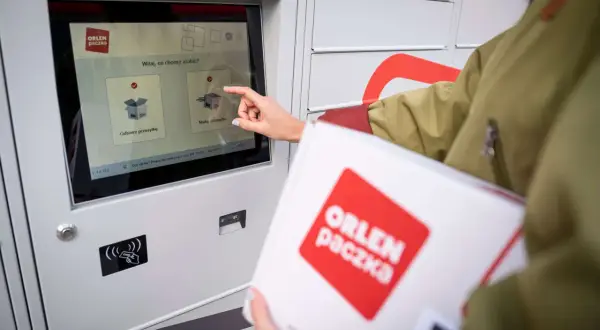 Kobieta odbiera paczkę z automatu ORLEN Paczka. Czy ORLEN Paczka dostarcza w soboty? Sprawdź na ekranie automatu.