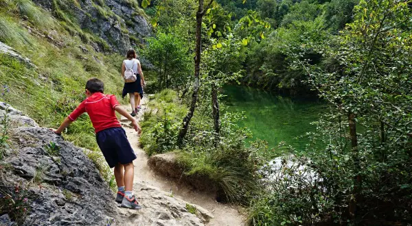 Niños exploran la senda de la hoya de san vicente, junto a un río de aguas cristalinas y vegetación exuberante.