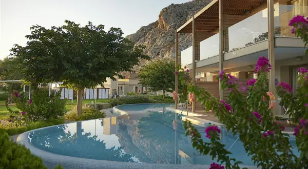 En vacker pool reflekterar bergen vid aegean park rhodos. Blommor och grönska omger hotellet.