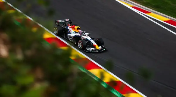 Liam Lawson compite en un coche de Fórmula 1 con los colores de Red Bull, acelerando en una curva con las marcas rojas y amarillas de la pista.