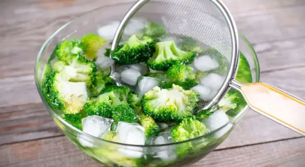 Frisch geschnittener Brokkoli wird in einer Eisschüssel abgekühlt, um das Brokkoli blanchieren zu perfektionieren. Ein Sieb hilft beim Herausnehmen.