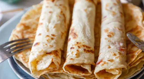 Drei goldbraune Pfannkuchen, aufgerollt und gestapelt, ein sehr gutes Pfannkuchen Rezept, bereit zum Genießen. Eine Gabel liegt daneben.
