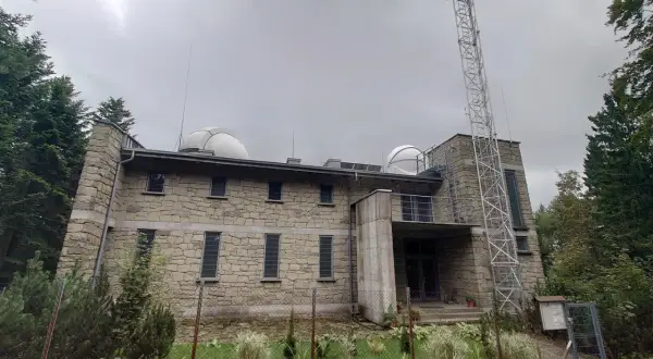 Obserwatorium na Lubomirze, kamienny budynek z kopułami i wieżą telekomunikacyjną, otoczony zielenią.