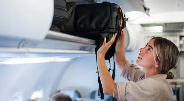 Junge Frau verstaut ihren großen Backpacking Rucksack im Gepäckfach eines Flugzeugs.