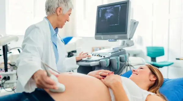Lekarka wykonuje USG brzucha uśmiechniętej pacjentki. To już 5 miesiąc ciąży, a na ekranie widać obraz dziecka.