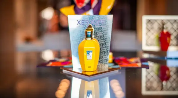 Żółta butelka perfum Xerjoff Erba Gold na lustrzanym blacie, odbijająca się w tafli.