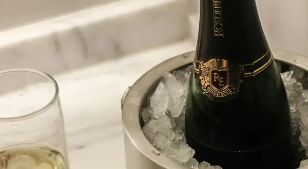 Eine Flasche Champagner in einem Eisbehälter, daneben ein Glas mit prickelndem Wein. Perfekt gekühlt, wann gefriert wein?