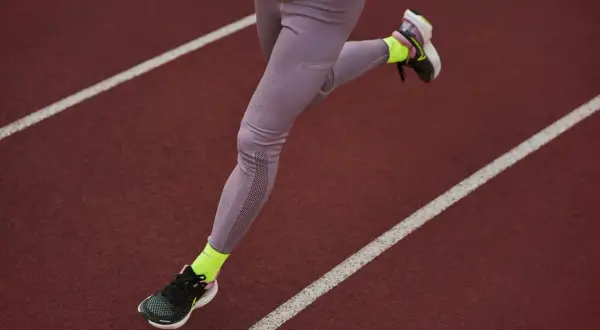 Une athlète court sur une piste, portant une chaussure de marche longue distance et des chaussettes fluo.
