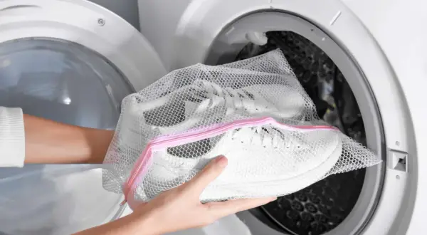 Mani inseriscono scarpe bianche in una retina per lavatrice. Attenzione: lavare le scarpe in lavatrice rovina la lavatrice.