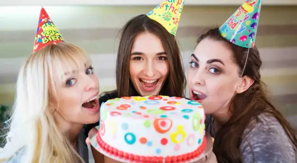 Tre amiche festeggiano con una torta colorata, pronte a soffiare le candeline per un addio al nubilato indimenticabile.