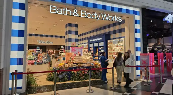 Sklep Bath & Body Works z promocjami, wystawą kwiatów i klientami.