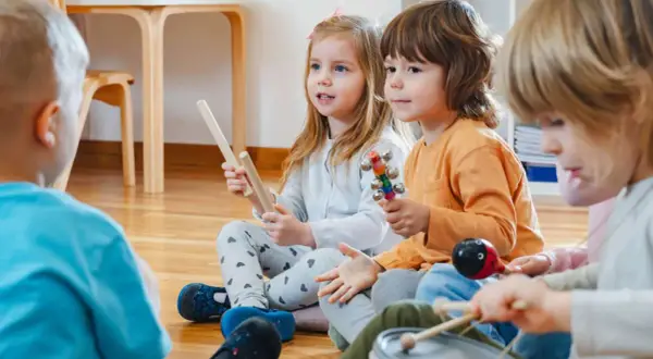 Kinder in der Kita lauschen gespannt einer Klanggeschichte und spielen mit Instrumenten.