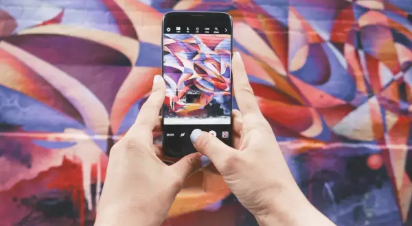 Zdjecie na Instagrama: ręce trzymają telefon, robiąc zdjęcie kolorowego muralu.