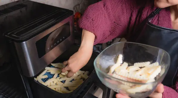 Ręka wkłada frytki do frytkownicy, przygotowując pyszne dania z airfryer przepisy po polsku.