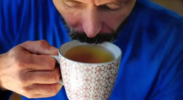 Mężczyzna w niebieskim swetrze pije napar z ziół na refluks z ozdobnego kubka.
