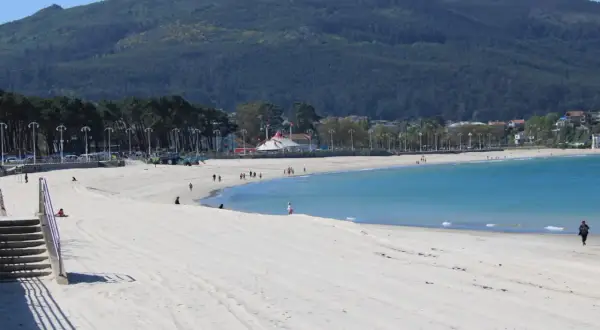 Amplia playa de arena blanca en la playa de Samil, con aguas turquesas y una montaña verde al fondo.