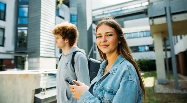 Zwei Studierende vor moderner Architektur. Sie lächelt in die Kamera, er blickt zur Seite. Ist die IU privat?