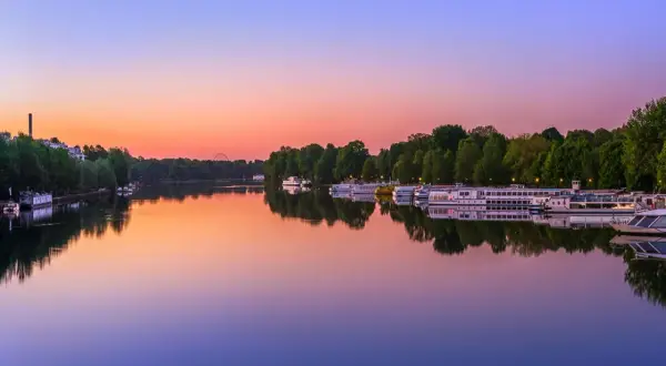 Boote liegen im Wasser vor dem grünen Ufer des Treptower Parks im Abendrot.