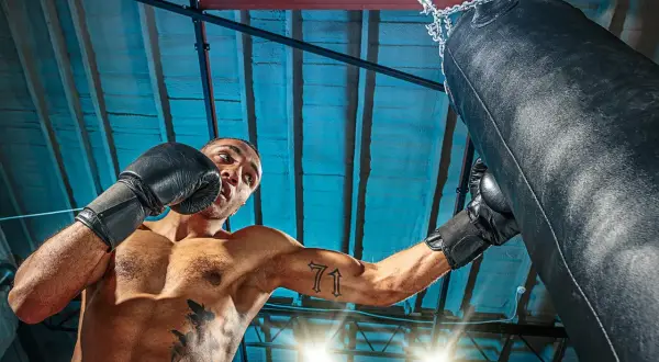 Man i boxningshandskar tränar sparra boxning mot en sandsäck i ett gym.